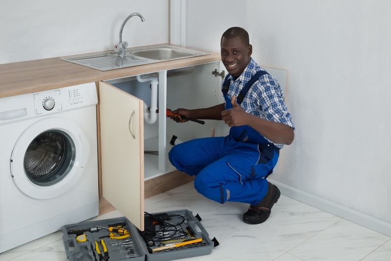 young happy african male plumber fixing sink in kitchen